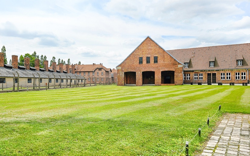Auschwitz Birkenau barracks and main building with green lawn in foreground.
