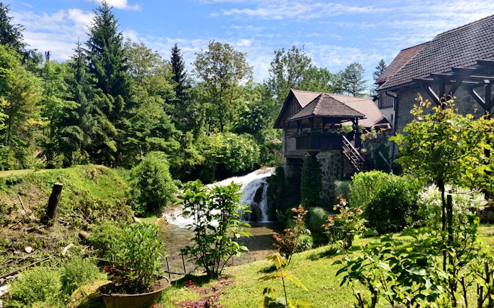Waterfall and rustic house in lush greenery at Rastoke Village, Croatia.