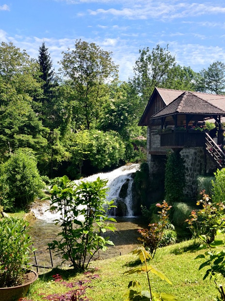 Waterfall and rustic house in lush greenery at Rastoke Village, Croatia.
