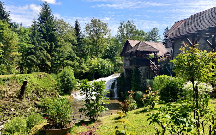 Waterfall and rustic house in lush greenery at Rastoke Village, Croatia.