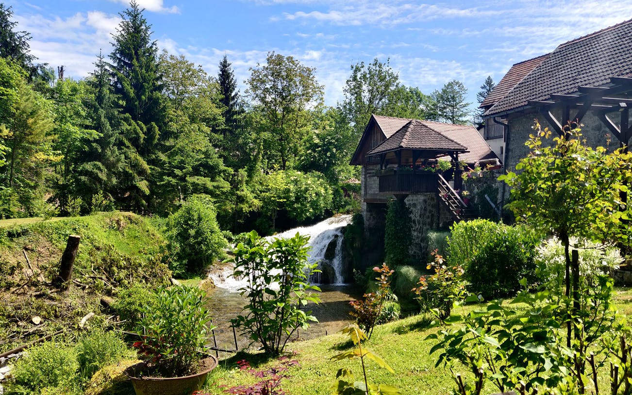 Waterfall and rustic house in lush greenery at Rastoke Village, Croatia.