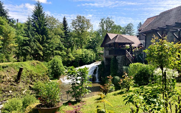 Waterfall and rustic house in lush greenery at Rastoke Village, Croatia.