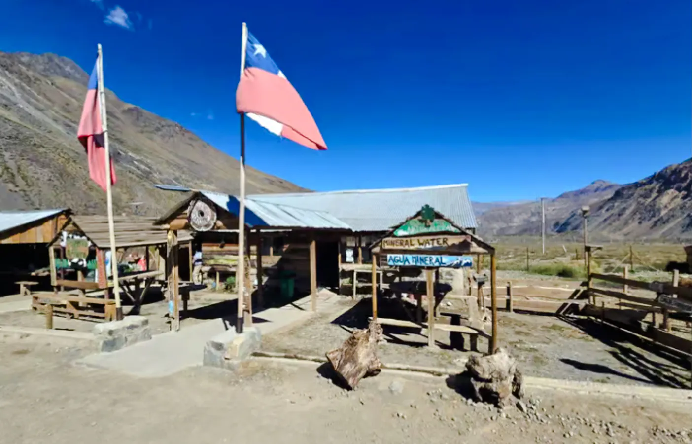 Rustic wooden cabin with Chilean flags in Cajón del Maipo, Santiago, offering mineral water.
