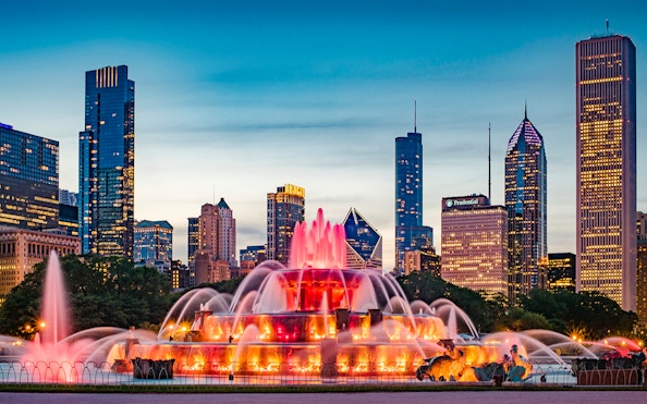 Buckingham Fountain illuminated at dusk with Chicago skyline in the background.