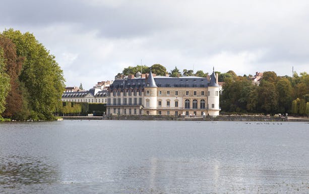 Castle of Rambouillet by a lake surrounded by trees in France.