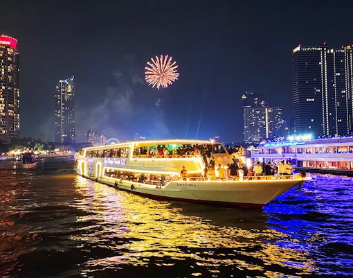 Dinner cruise on Chao Phraya River with fireworks and city skyline in Bangkok.