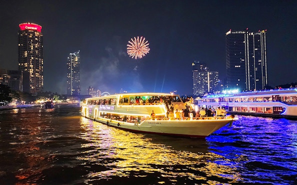 Dinner cruise on Chao Phraya River with fireworks and city skyline in Bangkok.