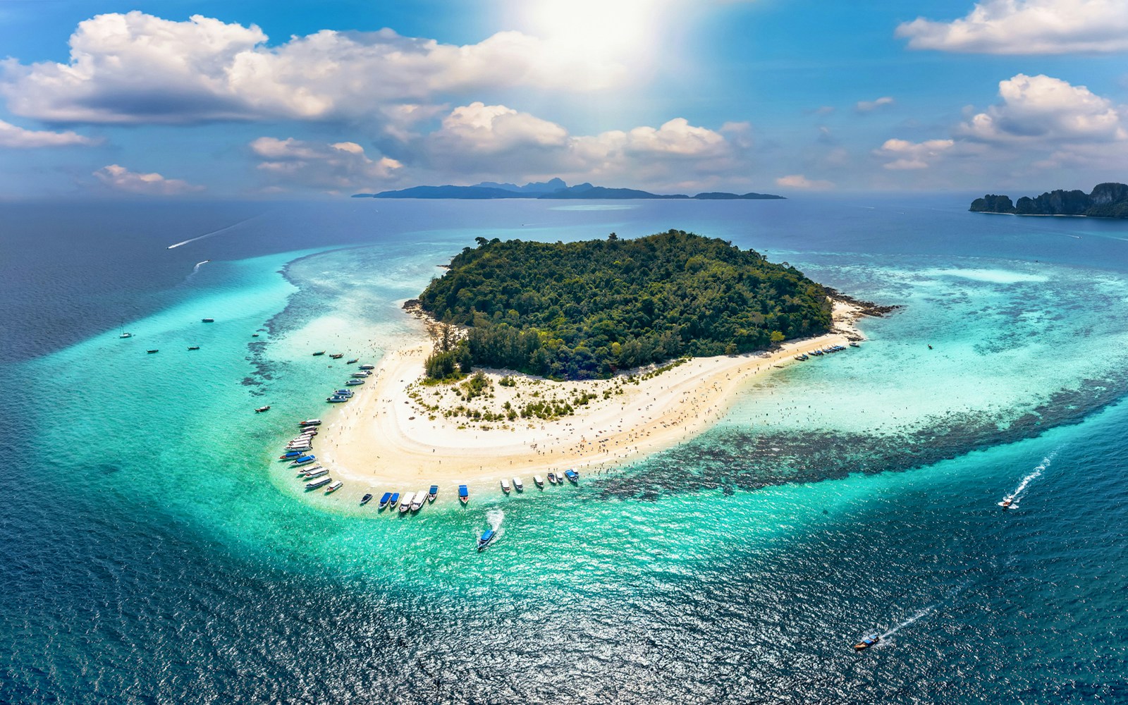 Aerial view of Bamboo Island with boats along the sandy shore and turquoise waters.