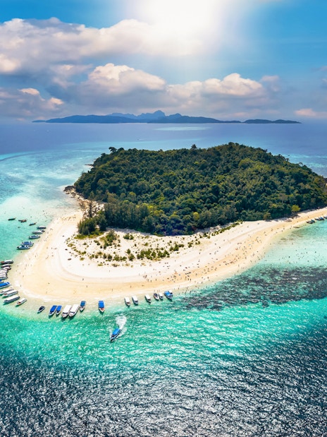 Aerial view of Bamboo Island with boats along the sandy shore and turquoise waters.