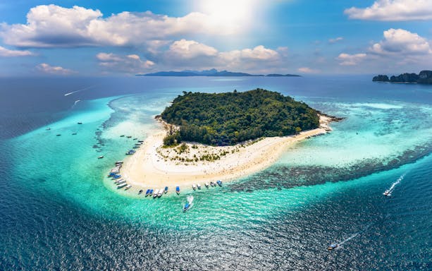 Aerial view of Bamboo Island with boats along the sandy shore and turquoise waters.
