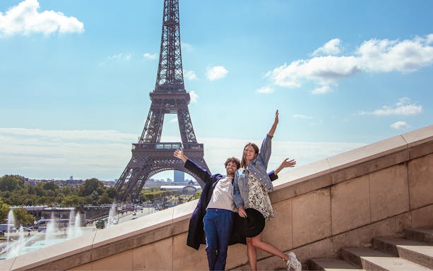 Couple posing joyfully in front of the Eiffel Tower during a private photoshoot in Paris.