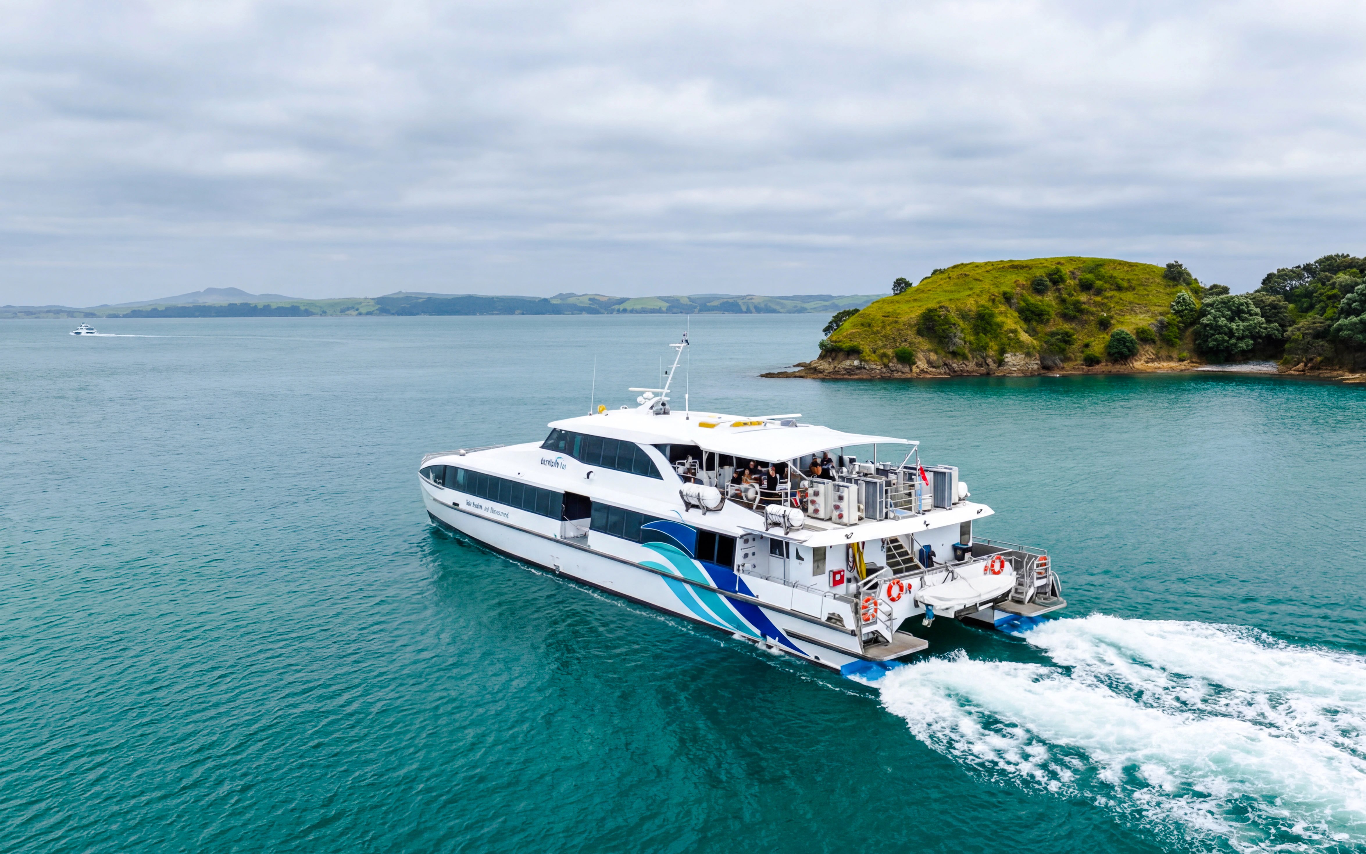 Ferry approaching Rangitoto Island from Auckland across blue waters.