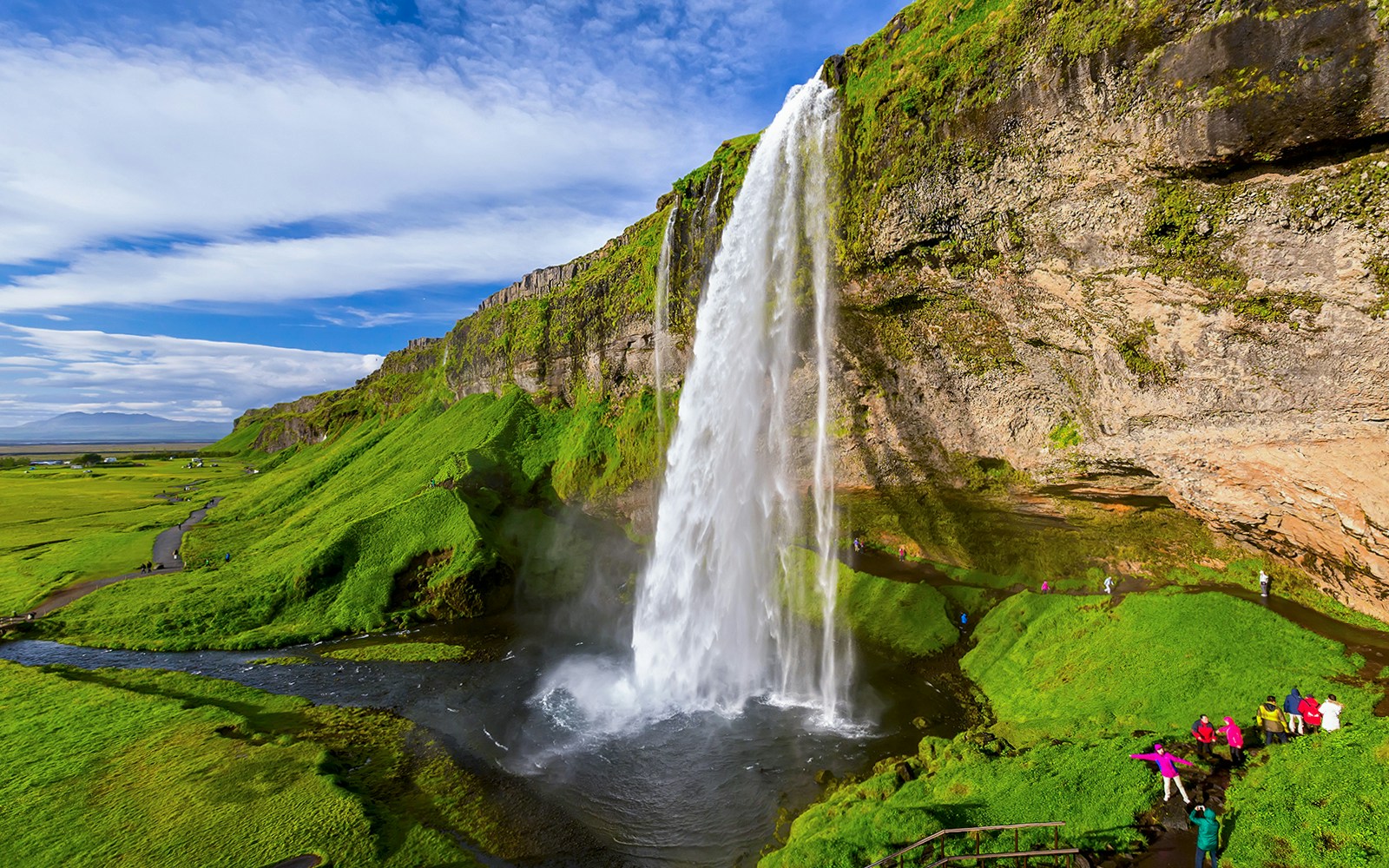 Seljalandsfoss Waterfall in Iceland with tourists walking behind the cascading water.