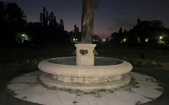 Fountain with statue in Les Jardins, Bucharest, at dusk during self-guided city exploration game.