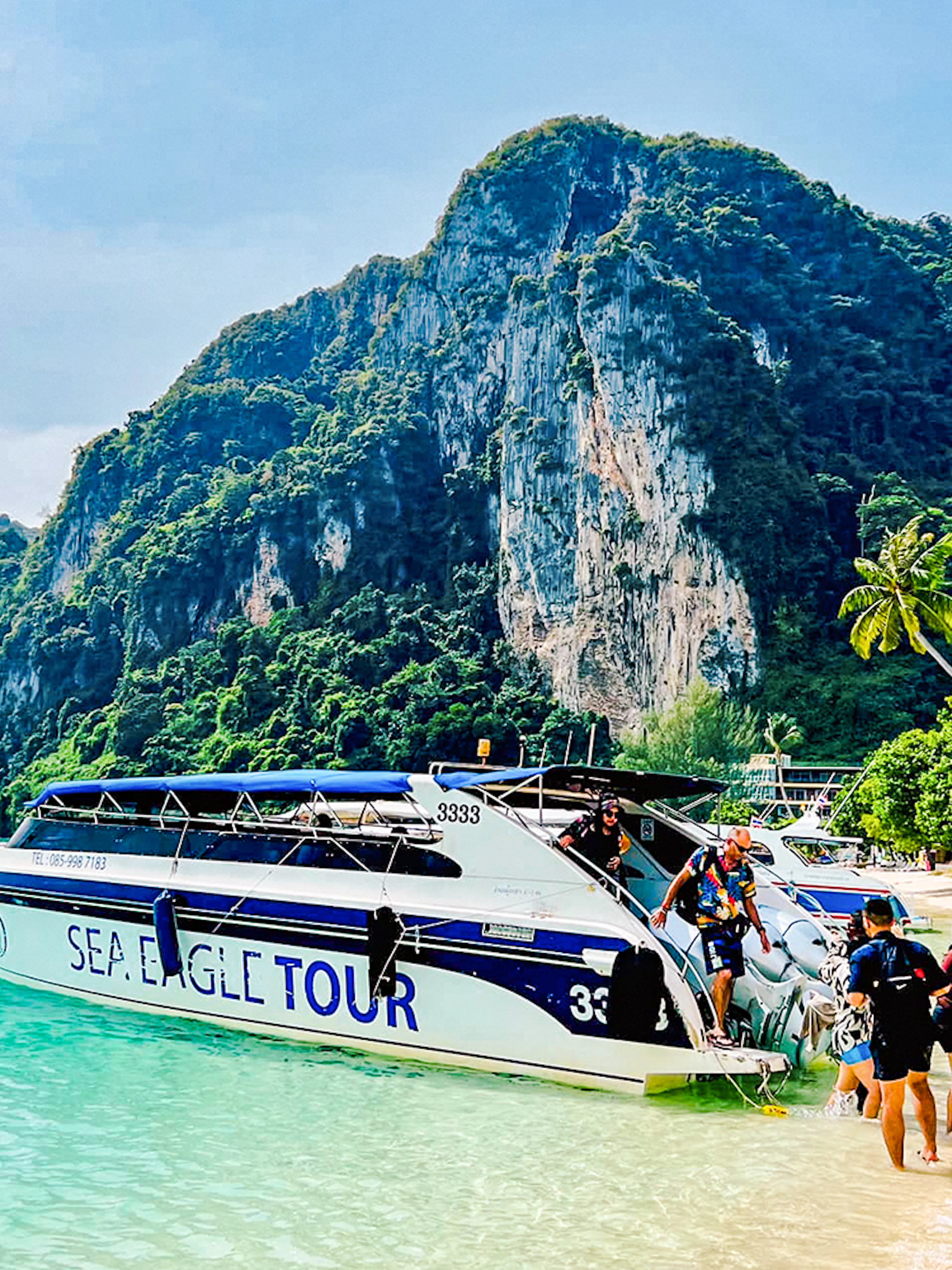 Boat tour arriving at Phi Phi Islands beach with limestone cliffs in the background.