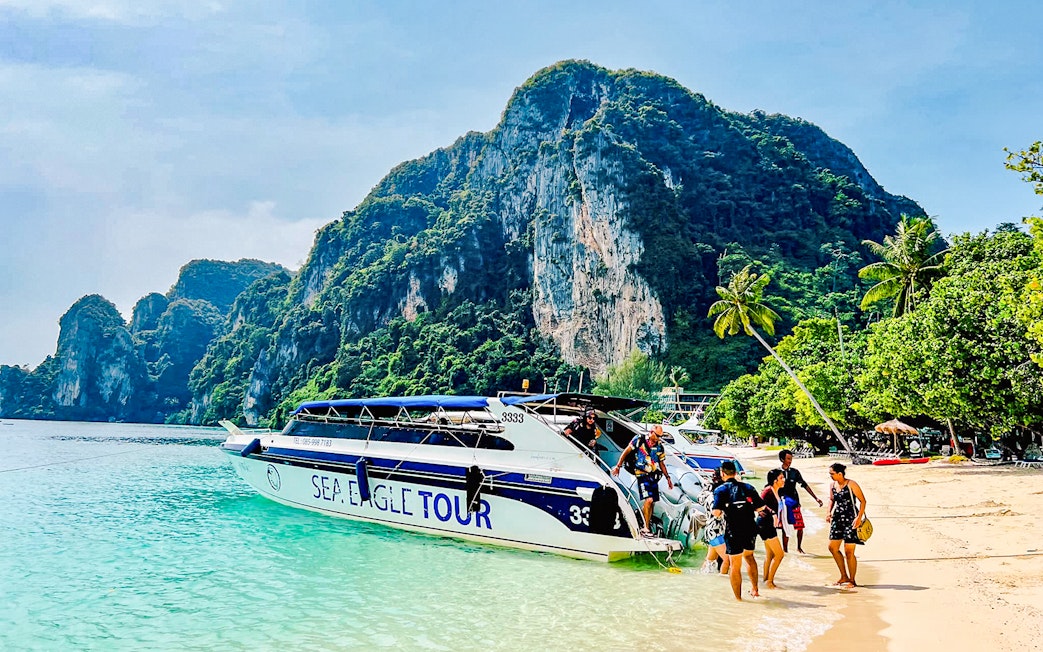 Boat tour arriving at Phi Phi Islands beach with limestone cliffs in the background.