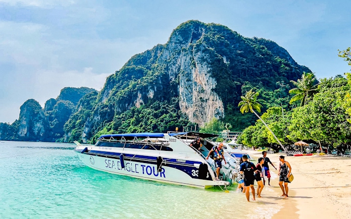 Boat tour arriving at Phi Phi Islands beach with limestone cliffs in the background.