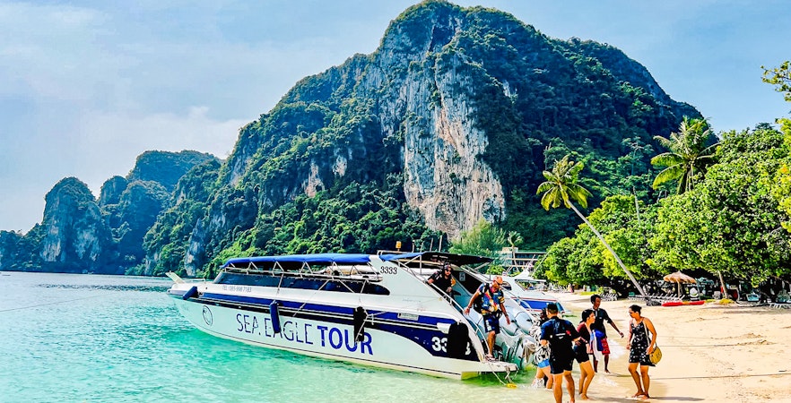Boat tour arriving at Phi Phi Islands beach with limestone cliffs in the background.