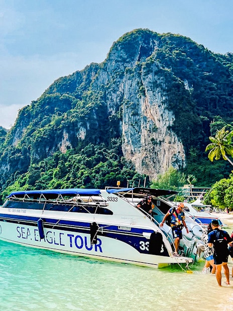 Boat tour arriving at Phi Phi Islands beach with limestone cliffs in the background.