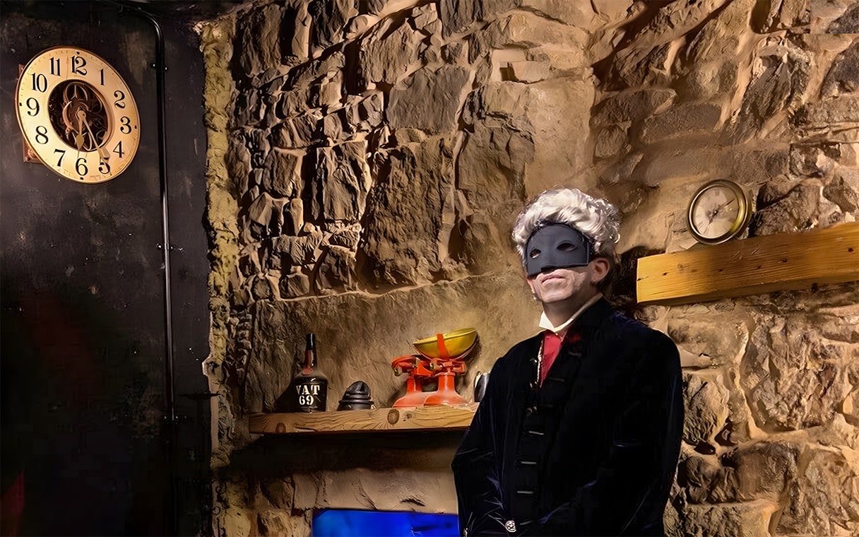 Masked figure in historical attire in a dimly lit stone room, part of Extreme Paranormal Activity Tour.