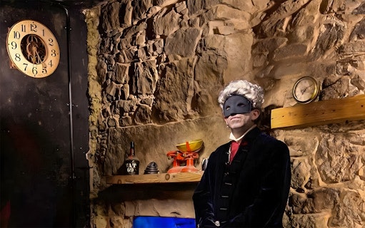 Masked figure in historical attire in a dimly lit stone room, part of Extreme Paranormal Activity Tour.