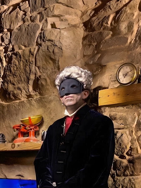 Masked figure in historical attire in a dimly lit stone room, part of Extreme Paranormal Activity Tour.
