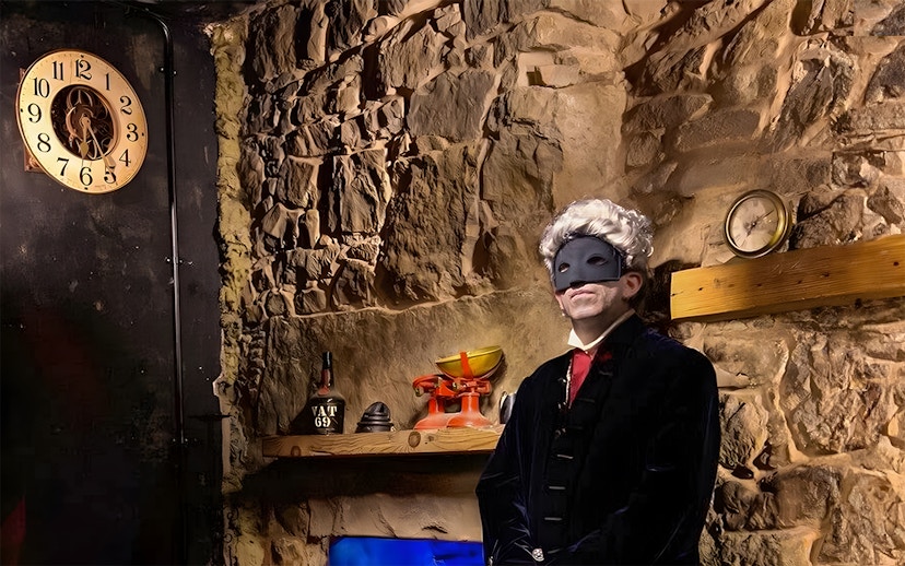 Masked figure in historical attire in a dimly lit stone room, part of Extreme Paranormal Activity Tour.