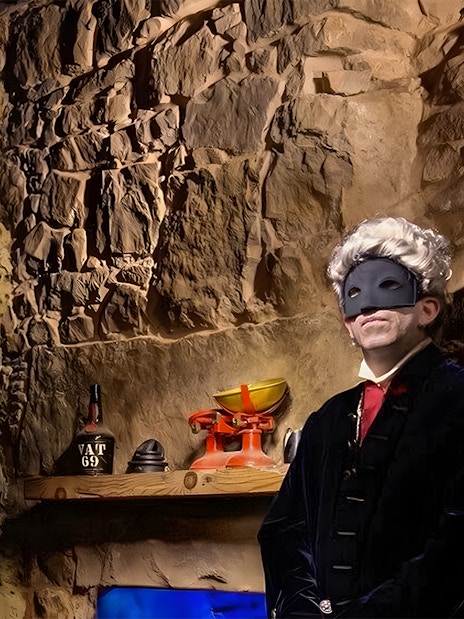 Masked figure in historical attire in a dimly lit stone room, part of Extreme Paranormal Activity Tour.