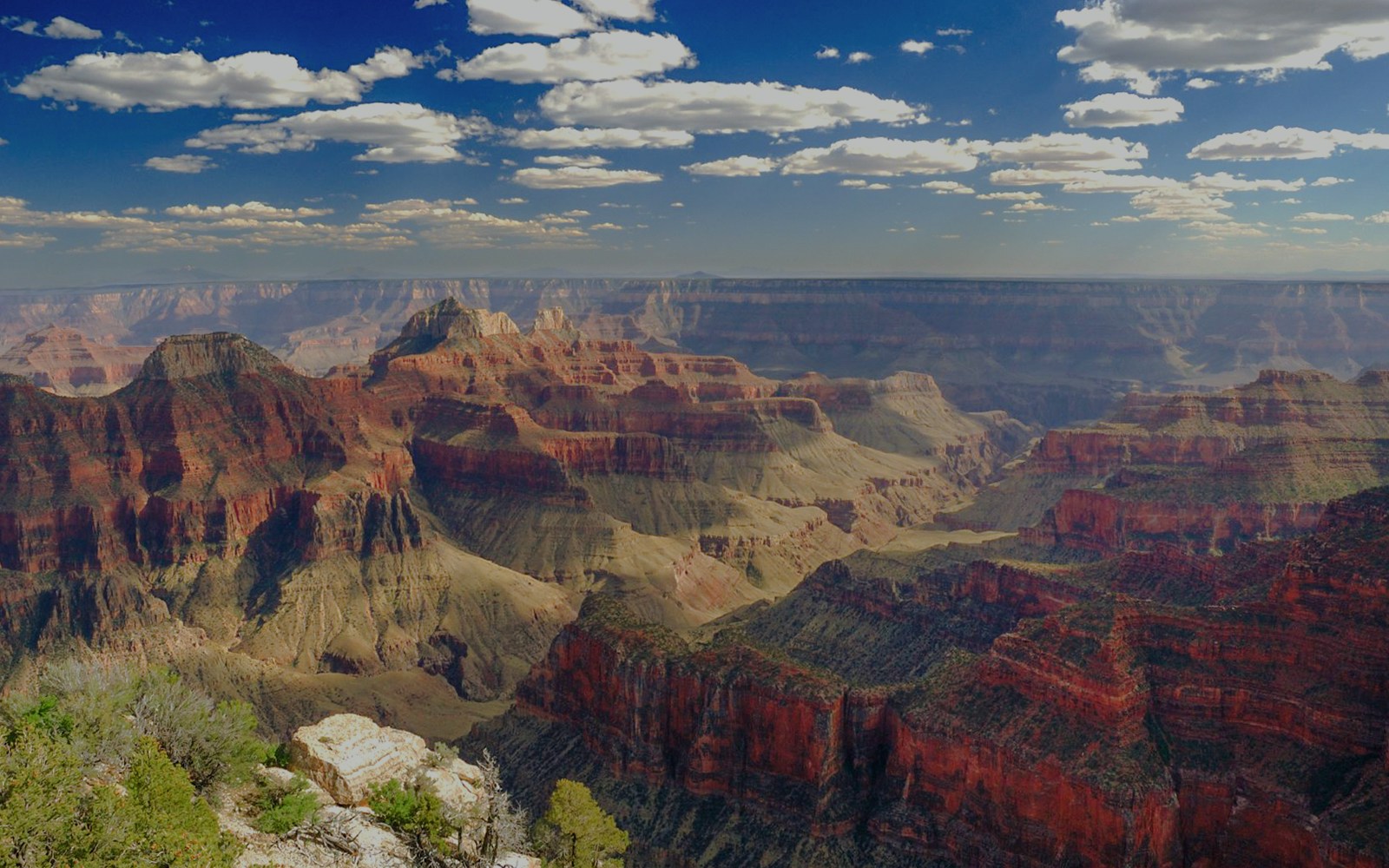 Grand Canyon panoramic view with layered rock formations under a blue sky.