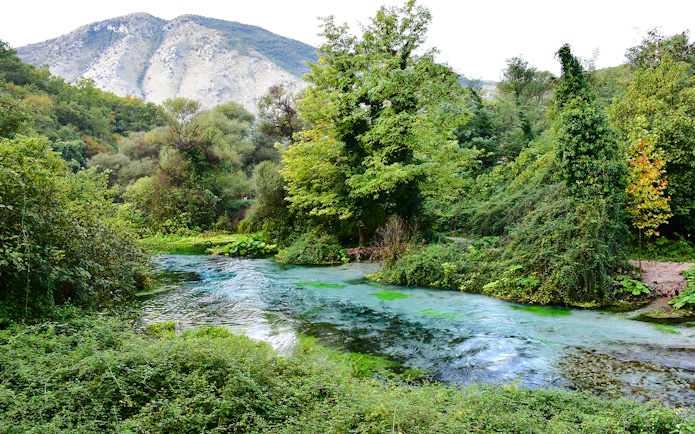 Blue Eye spring surrounded by lush greenery and mountains in Albania.