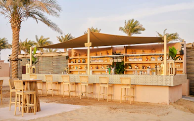 Bar area at Noble Camp Desert Safari with stools and palm trees.