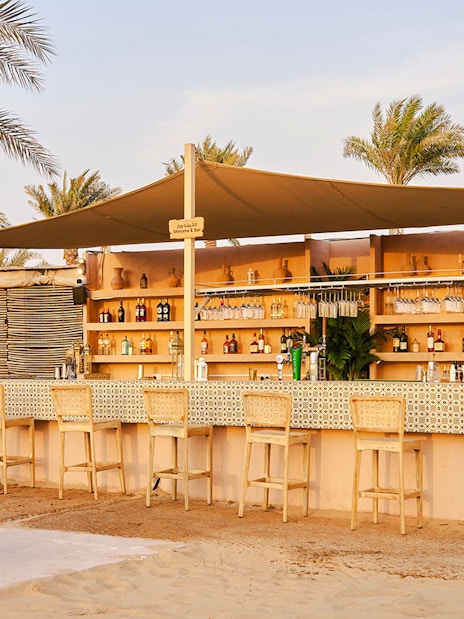 Bar area at Noble Camp Desert Safari with stools and palm trees.
