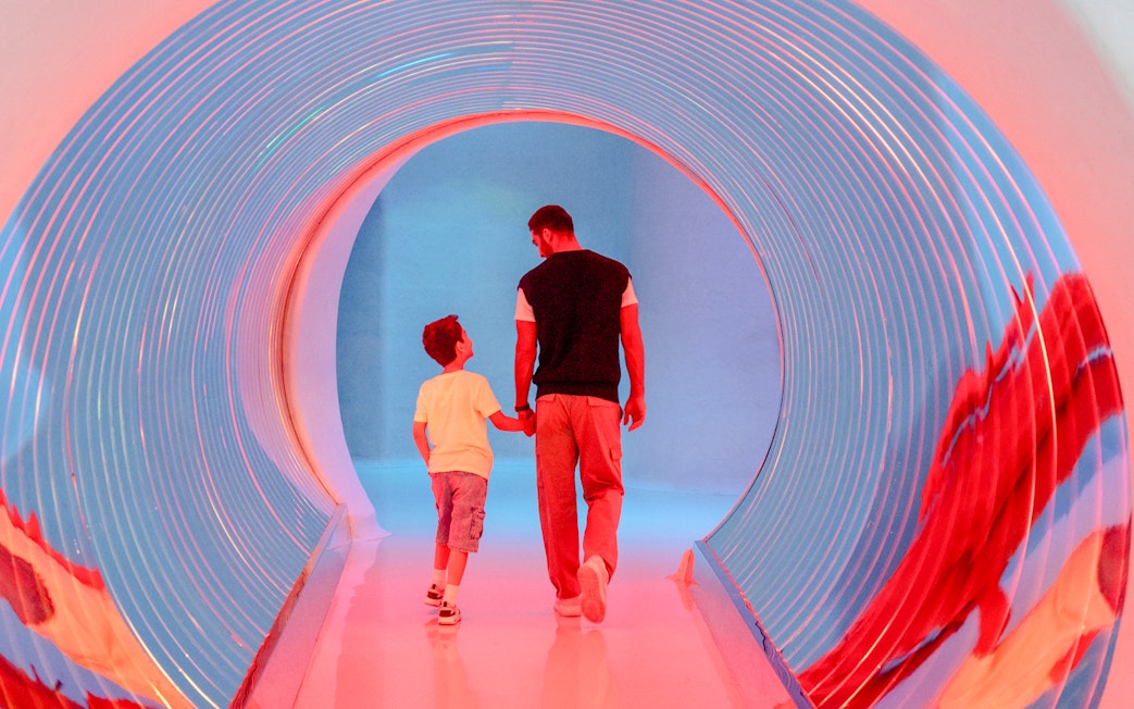 Man and child walking through a colorful tunnel at AYA Universe, Dubai.