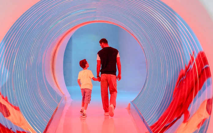 Man and child walking through a colorful tunnel at AYA Universe, Dubai.