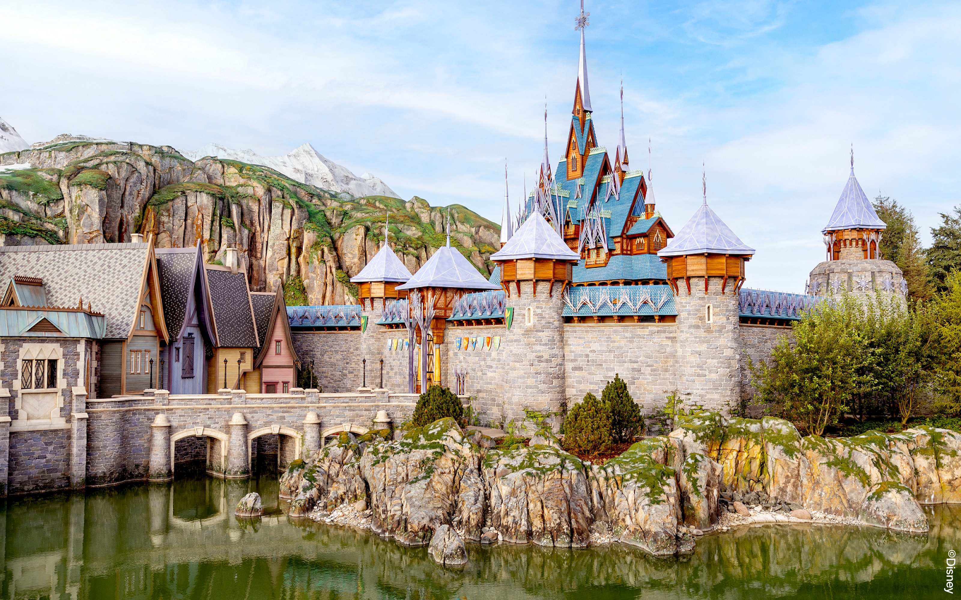 Disneyland Paris castle with stone bridge and mountain backdrop.