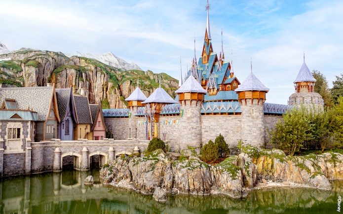 Disneyland Paris castle with stone bridge and mountain backdrop.