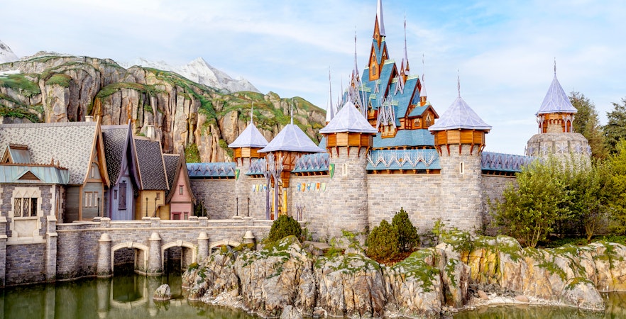 Disneyland Paris castle with stone bridge and mountain backdrop.