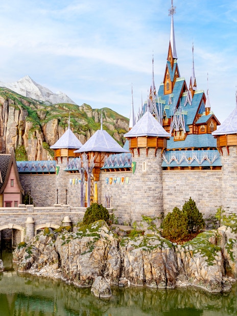 Disneyland Paris castle with stone bridge and mountain backdrop.