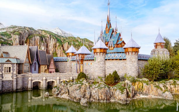 Disneyland Paris castle with stone bridge and mountain backdrop.