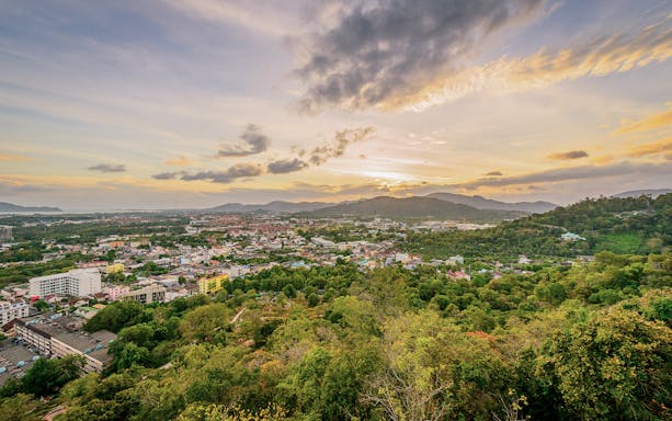 Phuket cityscape at sunset with lush greenery and distant mountains.