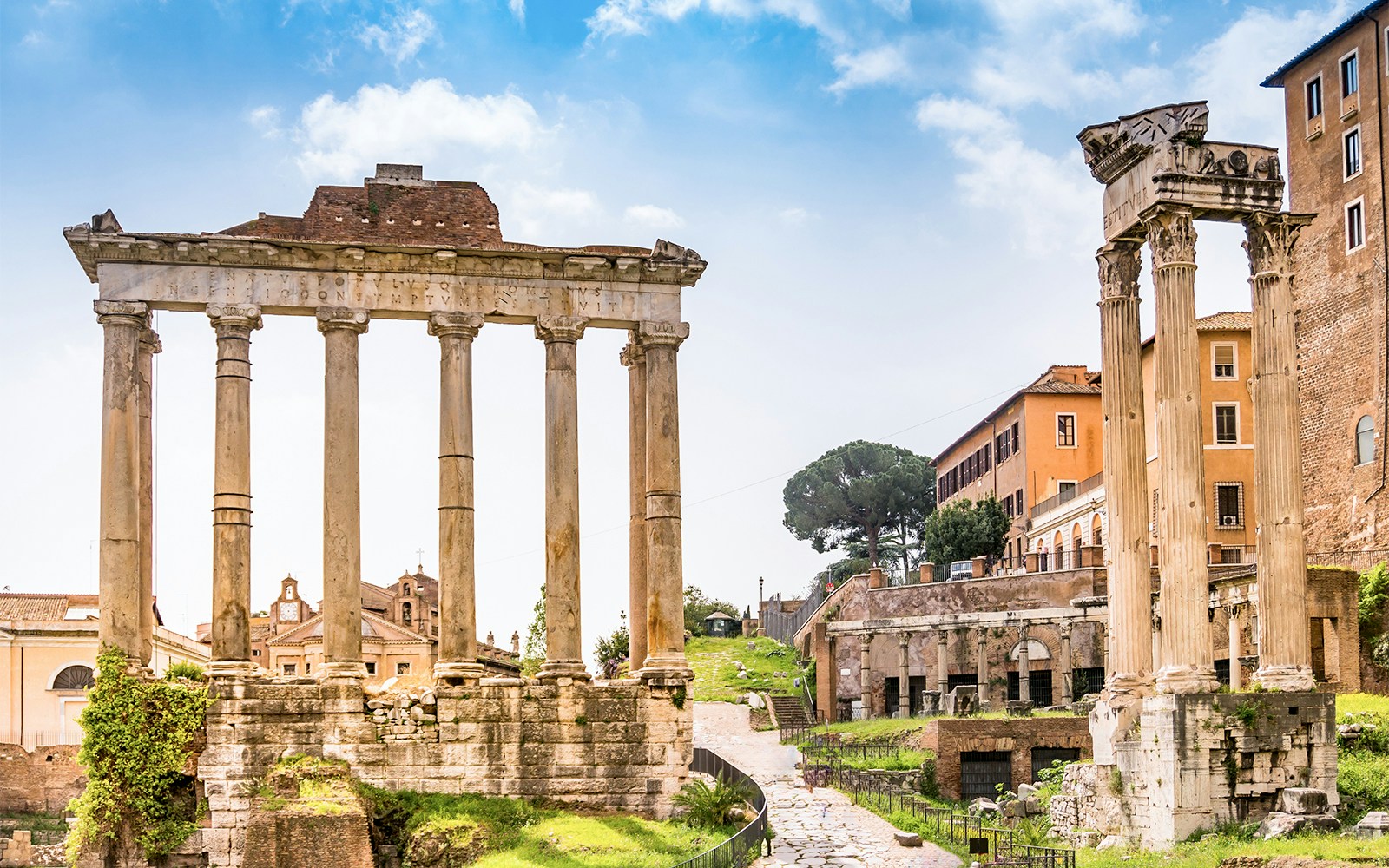 Roman Forum ruins with ancient columns and nearby historic buildings in Rome, Italy.
