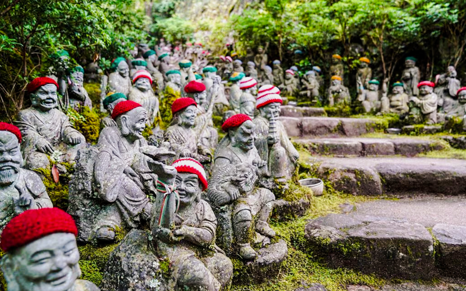Stone statues with red hats at Daishoin Temple, Japan, surrounded by greenery.