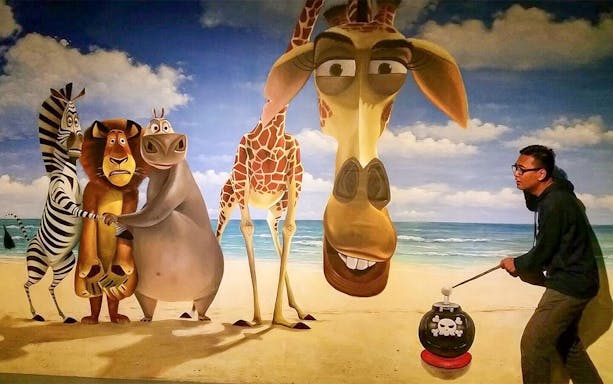 Man interacting with 3D art of animated animals on a beach at Alive 3D Art Gallery.
