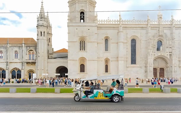 Tourist on eco tuk tuk passing Jeronimos Monastery in Lisbon.