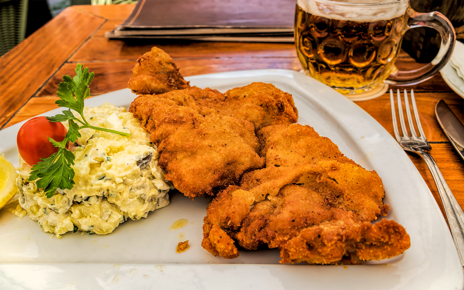 Wiener Schnitzel with potato salad and beer on a wooden table.