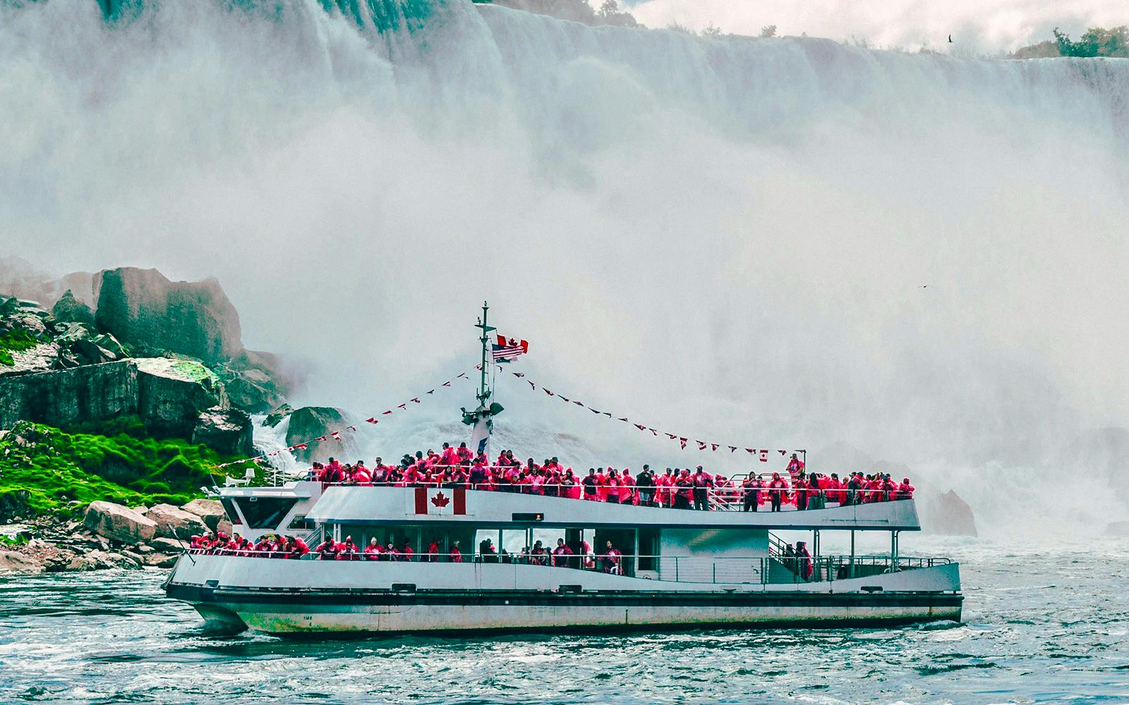 Tour boat approaching Niagara Falls, Canada with passengers in red raincoats.