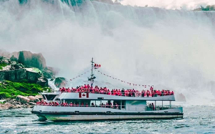 Tour boat approaching Niagara Falls, Canada with passengers in red raincoats.