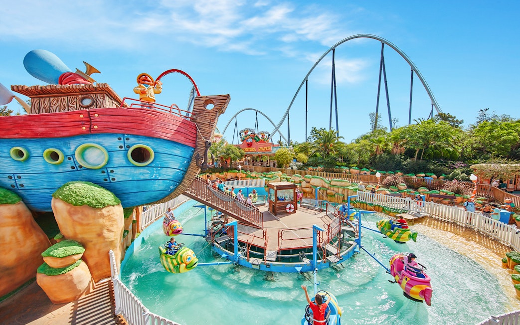 Colorful boat ride at PortAventura Park with roller coaster in background.