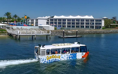 Quack'R Duck amphibious vehicle cruising on Gold Coast waterway near a waterfront hotel.