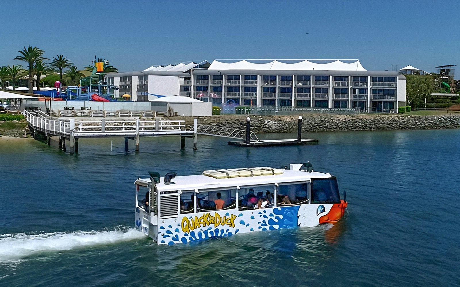 Quack'R Duck amphibious vehicle cruising on Gold Coast waterway near a waterfront hotel.